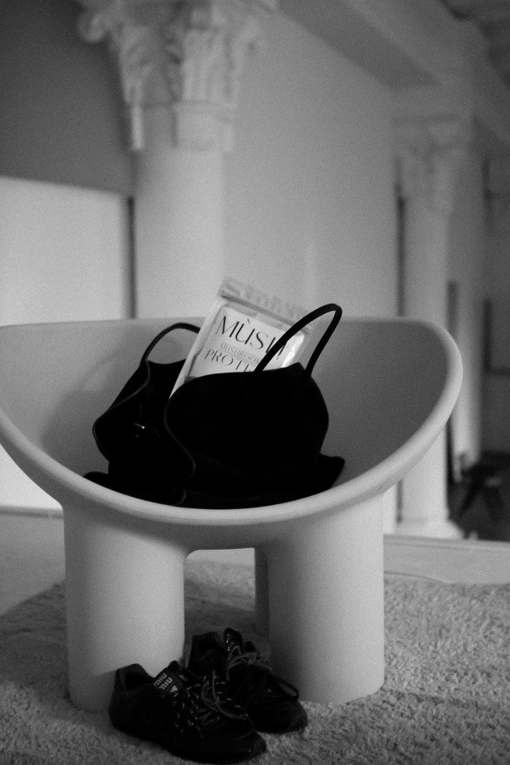 The Row black suede handbag on a Rolly Polly stool in a hall with architectural columns.